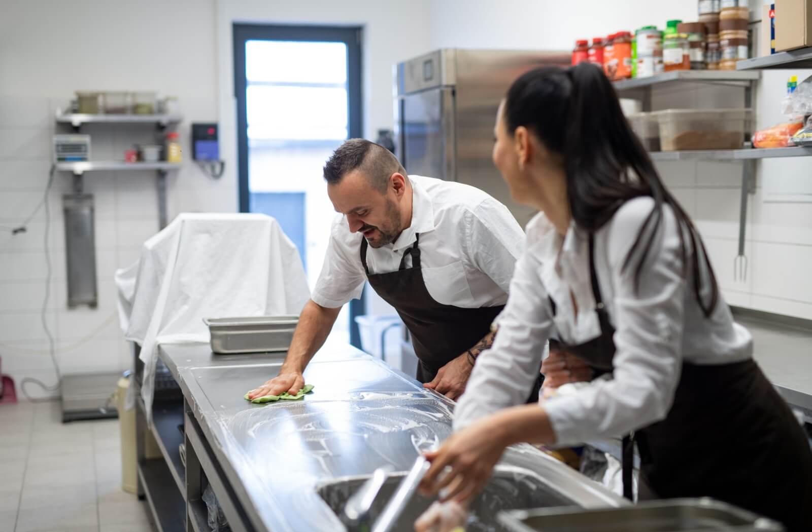 Two staff cleaning a commercial kitchen.