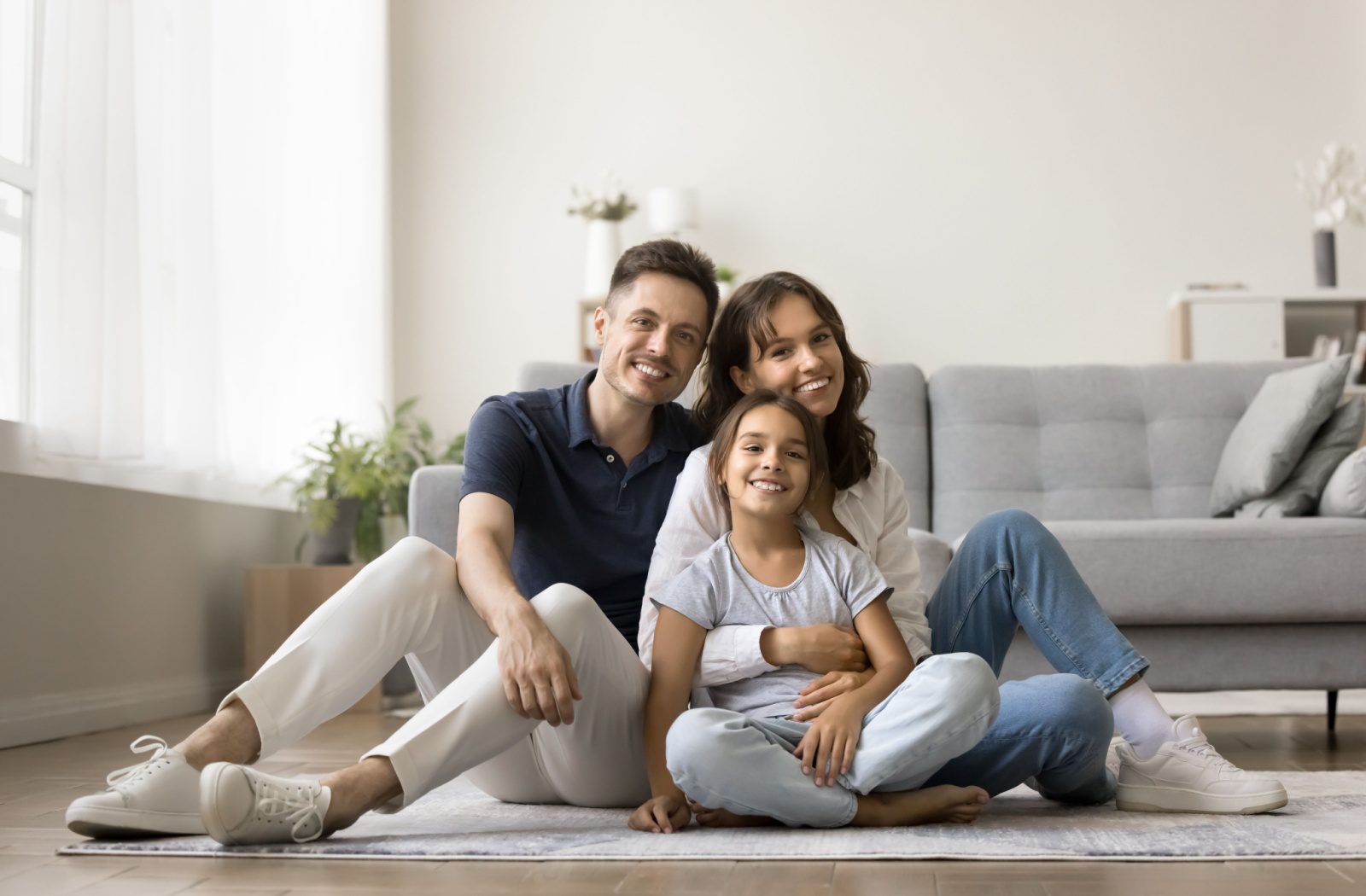 A young family sitting together on the carpet and smiling after having their home professionally cleaned.