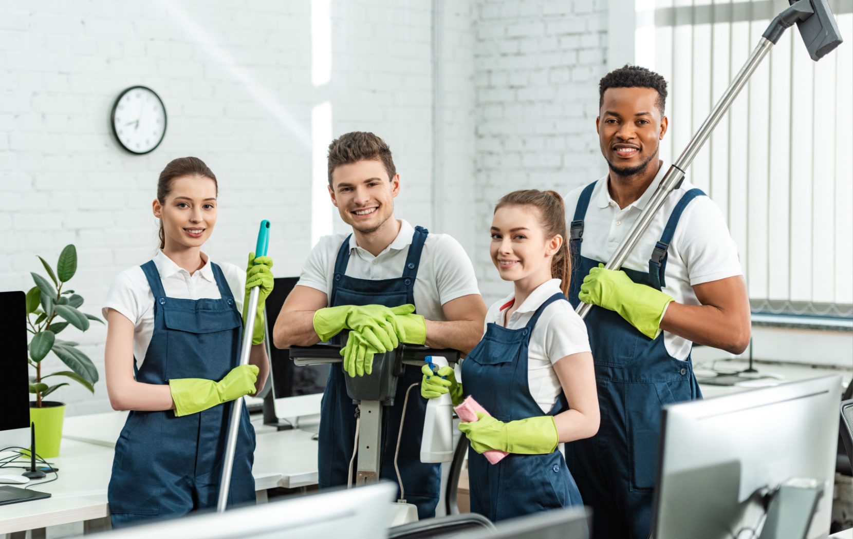 A professional cleaning crew wearing aprons and green gloves pause from cleaning to look up and smile.