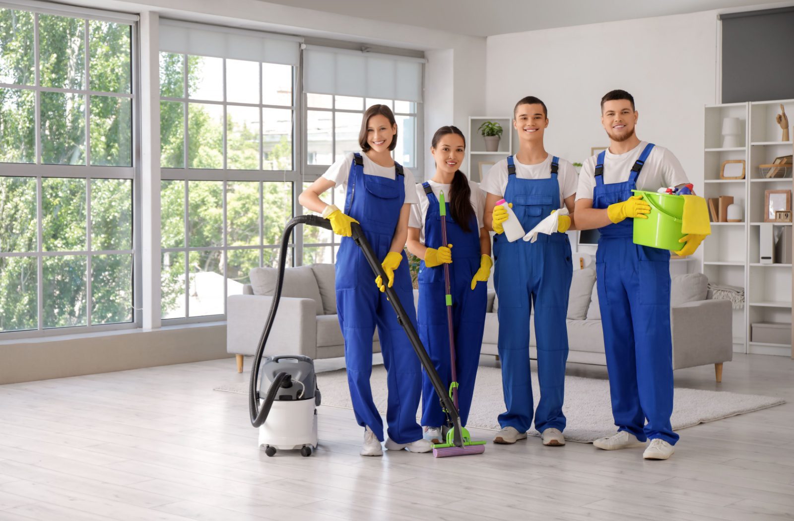 A happy team of move-out cleaners holding their equipment while standing side-by-side in a spotless living room.