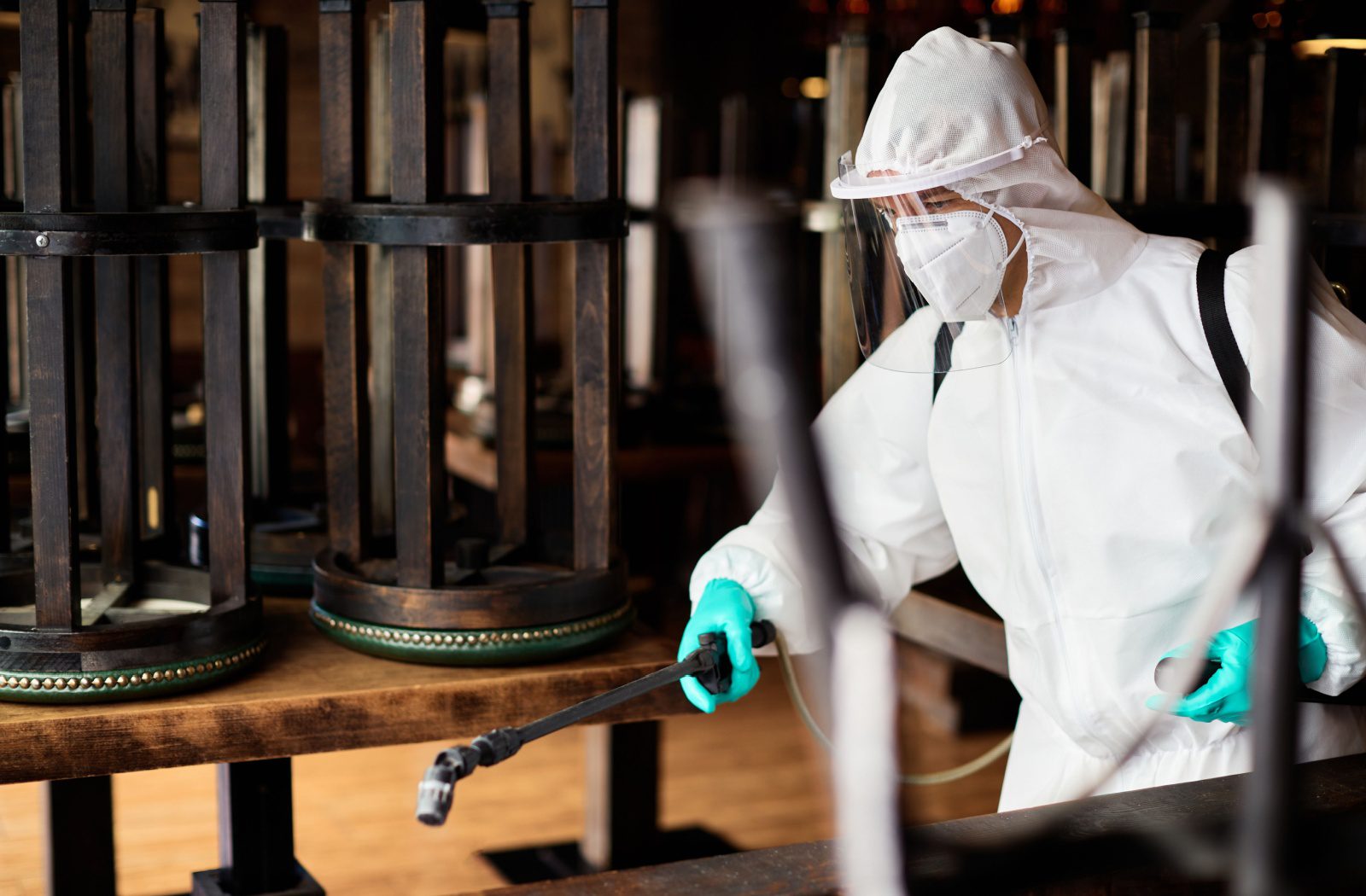 A person wearing protective gear sanitizes a restaurant's dining area.