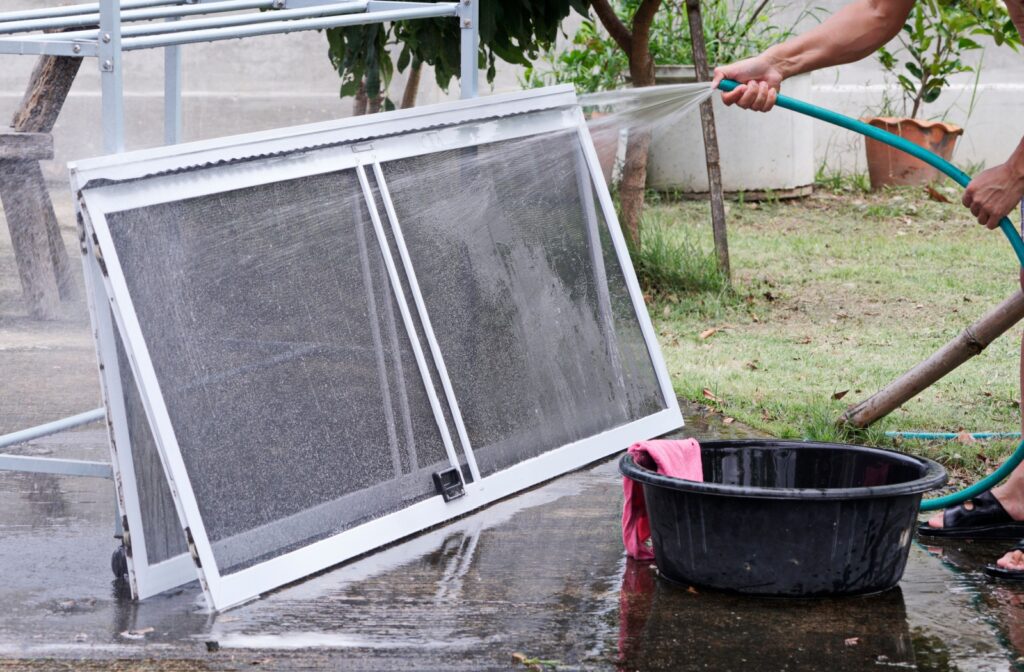A person off screen hosing down propped up window screens in a backyard.