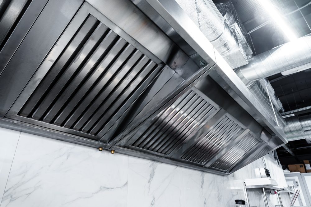 Clean stainless steel commercial kitchen exhaust hood with metal baffle filters installed above a cooking area.